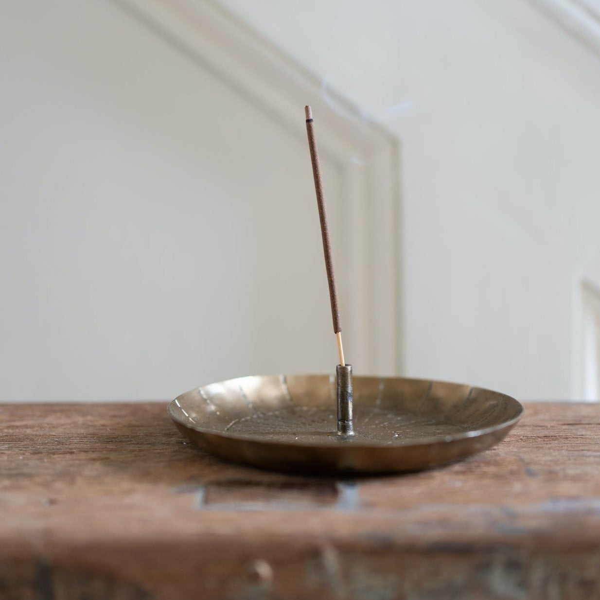 Brown incense stick burning in a brass incense holder on a wooden surface.