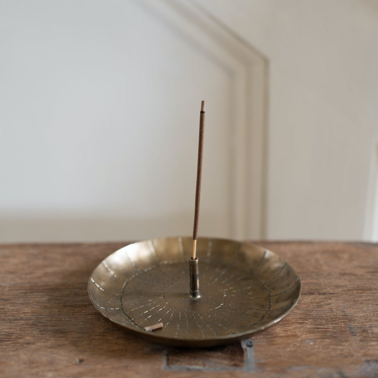 Incense stick burning in a brass incense holder with an etched circular design.