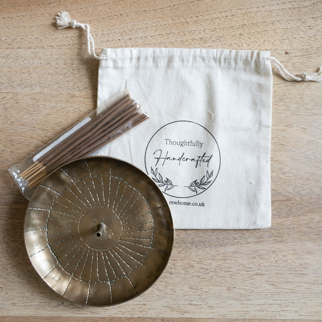 Brass incense holder with radiating design and a package of incense sticks beside a muslin bag.
