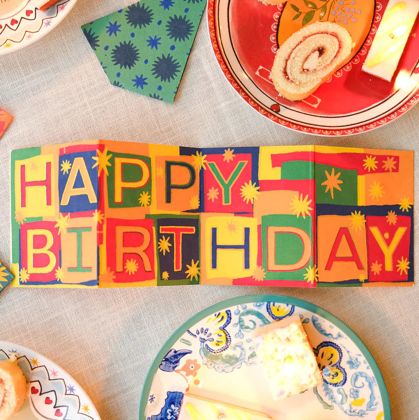 Colorful 'Happy Birthday' banner with plates and cake on a table.