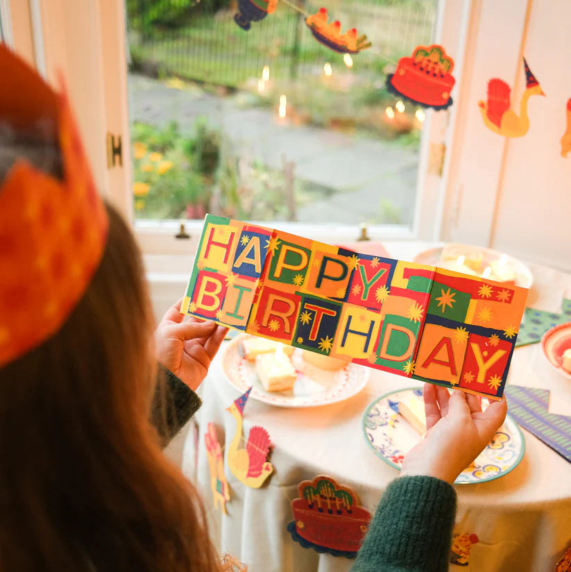 Person holding a colorful 'Happy Birthday' card at a birthday party.