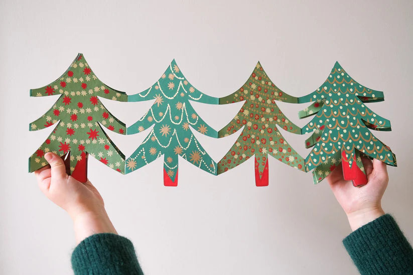 Two hands holding four paper Christmas trees with patterns on a plain background