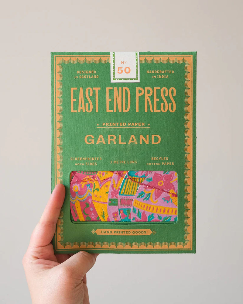 Hand holding a green box of East End Press Garland printed paper with colorful design on a light gray background