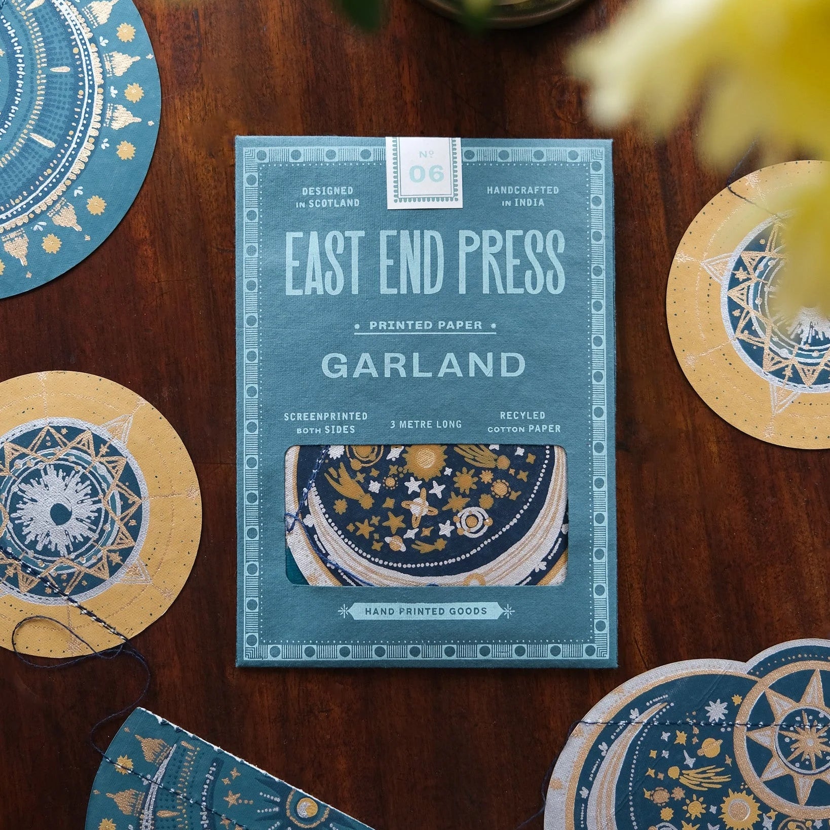 Packaging of East End Press Garland product on a wooden surface with decorative items.