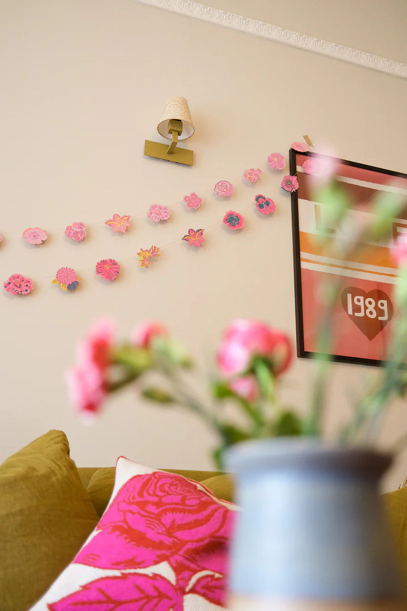 A paper flower garland with pink and yellow blooms decorates a wall.