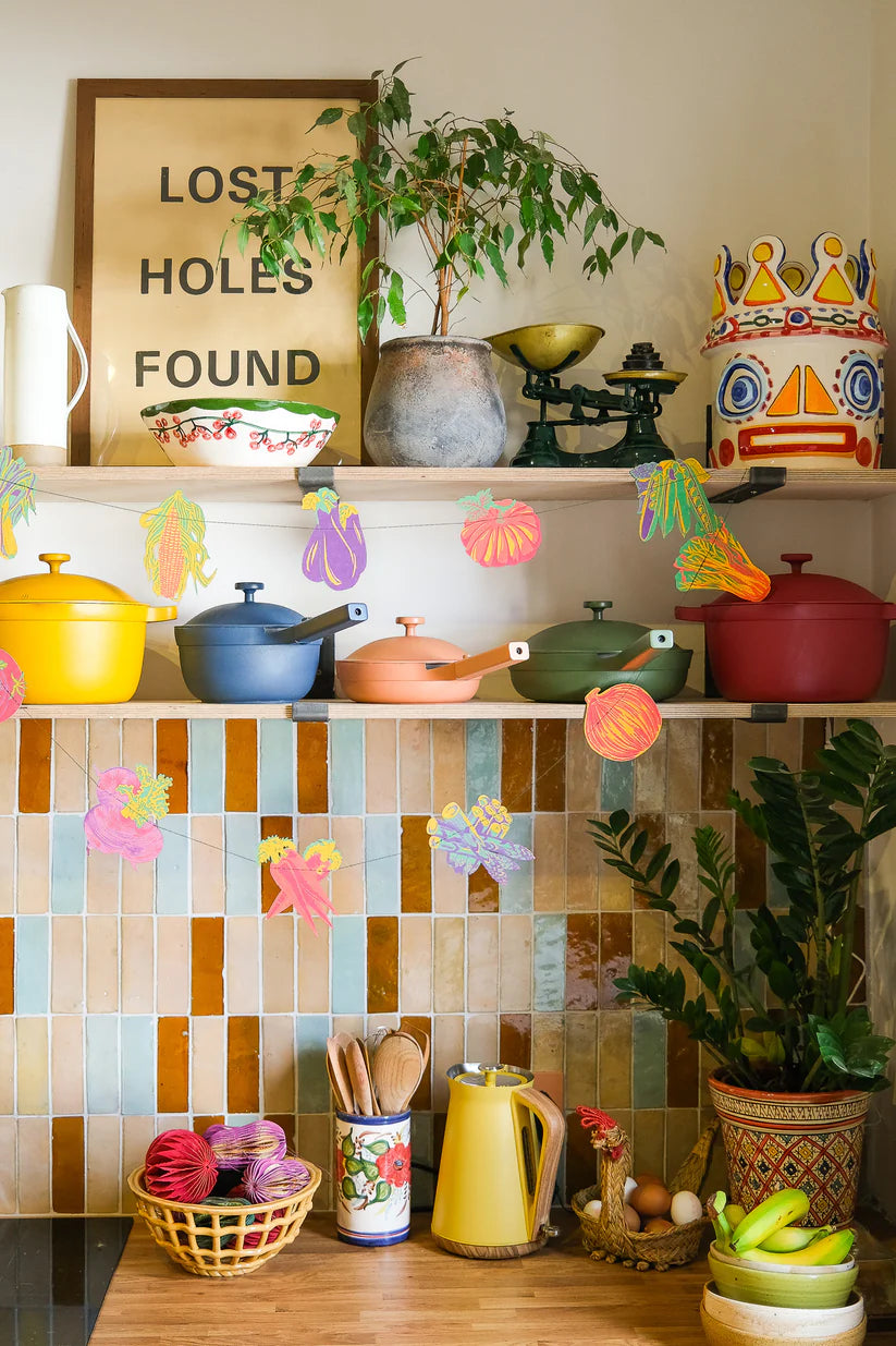 A collection of colorful enamel cookware sits on a shelf above a patterned tile backsplash.