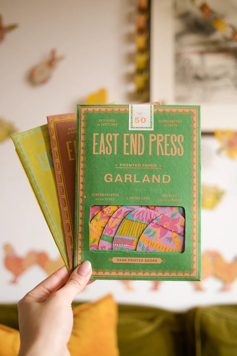 Hand holding a green box of East End Press Garland printed paper with colorful designs.