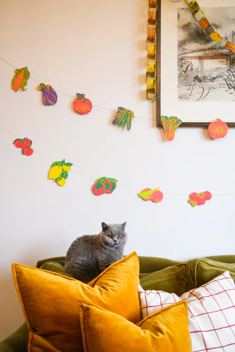 A colorful fruit and vegetable garland hangs on a wall.  The garland features various cut-out shapes of produce.