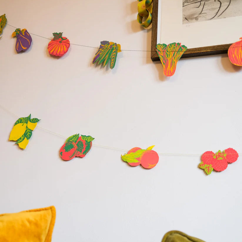 Fruit and vegetable garland with vibrant, stylized illustrations of lemons, peaches, raspberries, and other produce.