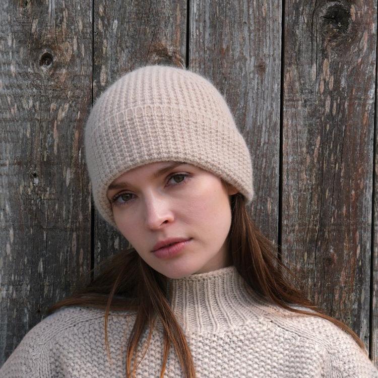 A light beige ribbed knit beanie.  The hat is shown on a model, against a wood background.