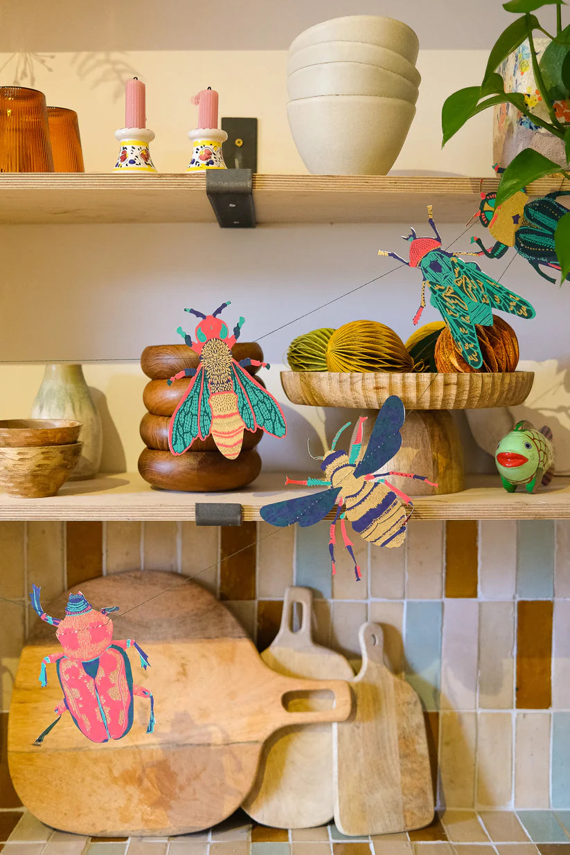 A string of colorful insect decorations hangs in a kitchen, featuring bees and beetles with intricate patterns.