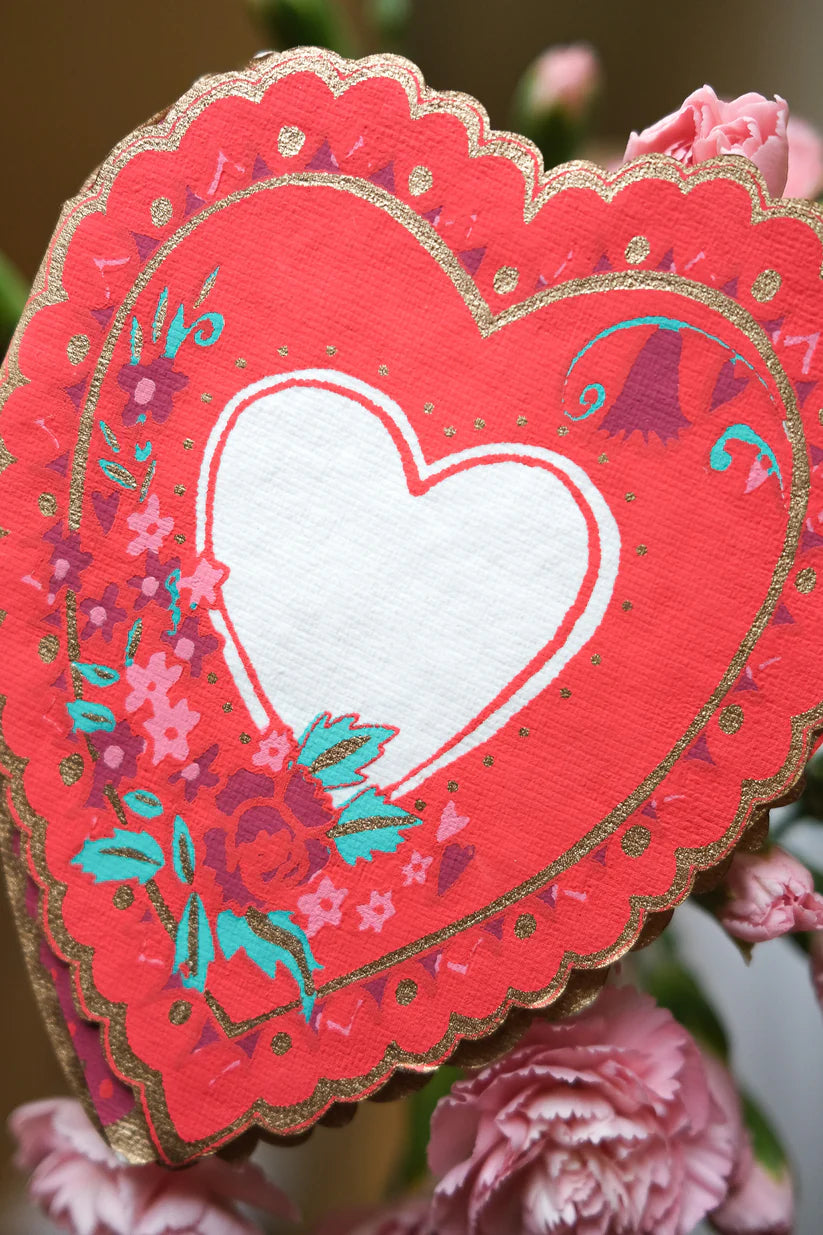 Red heart-shaped card with gold trim, featuring a smaller white heart in the center and pink floral details.