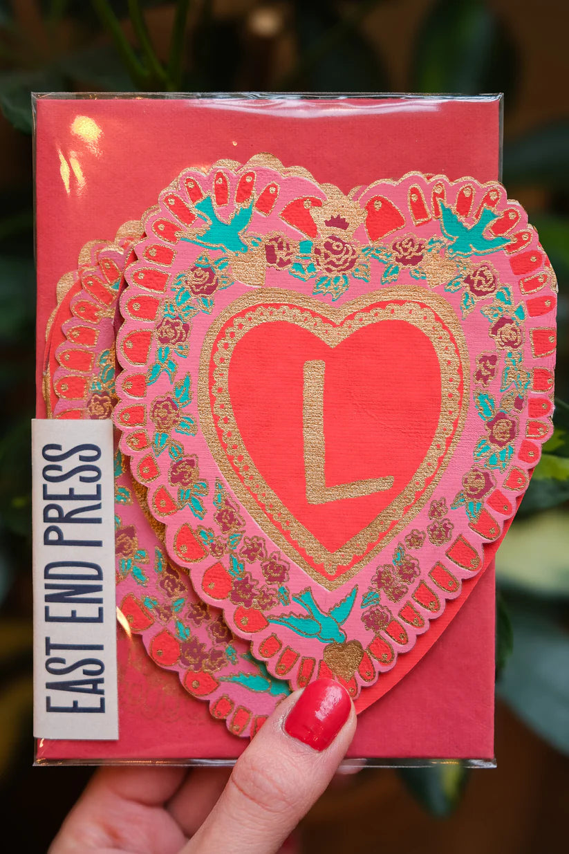 Layered pink heart-shaped cards with gold detailing and a gold "L" in the center.  The cards feature floral and bird designs.