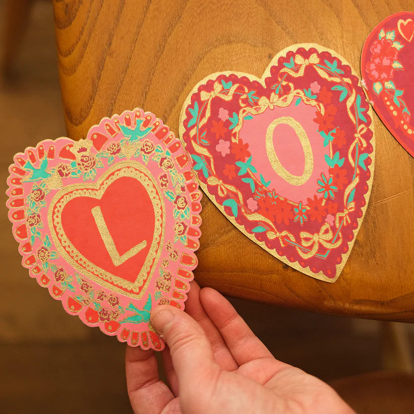 Heart-shaped Valentine's Day banner with gold detailing and letters "L" and "O" in pink and red.