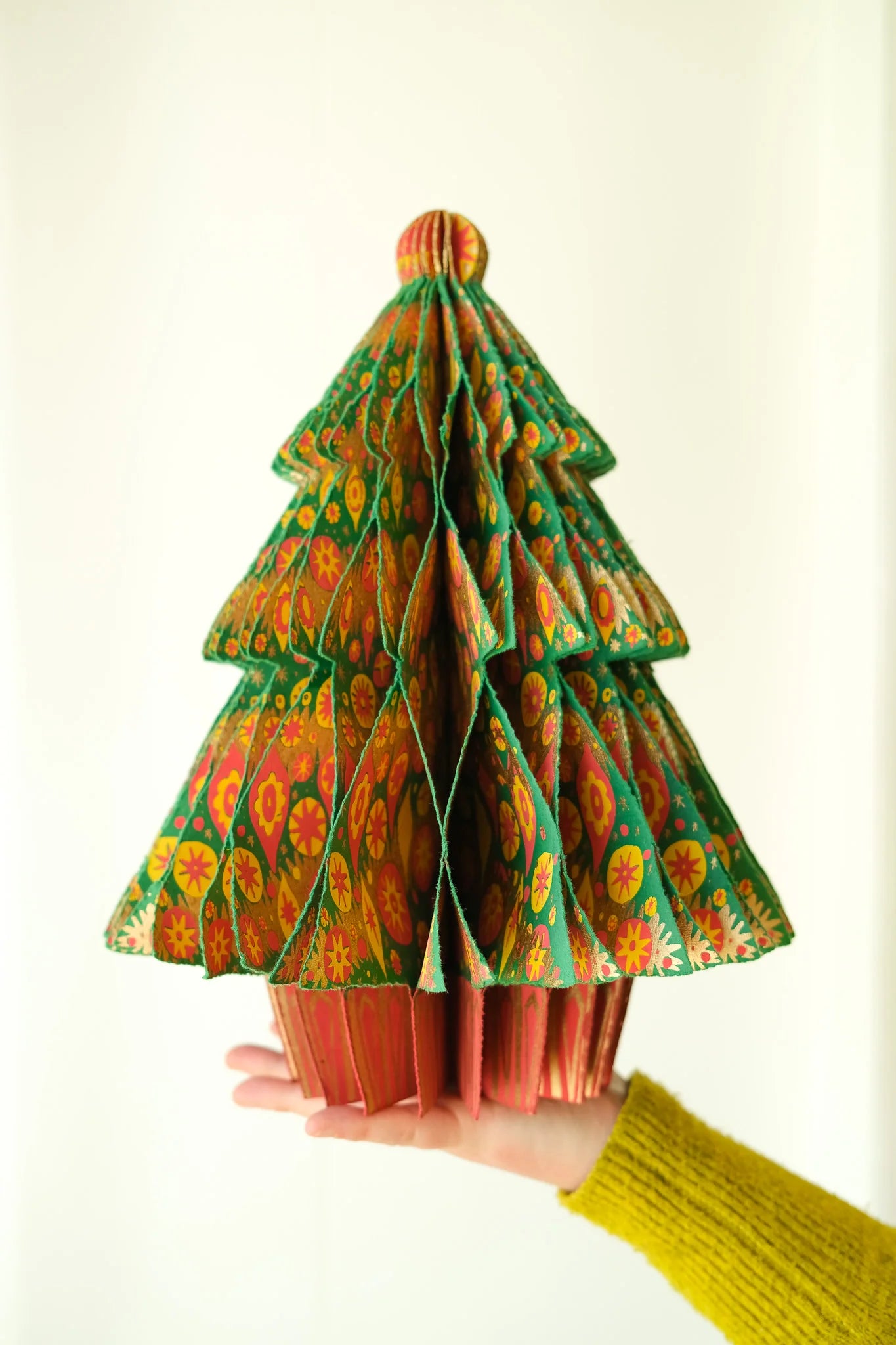 Hand holding a colorful folded paper tree against a white background