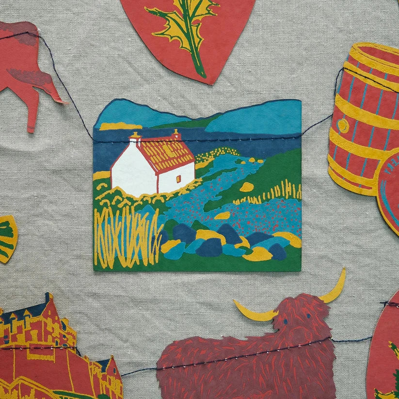 Stylized illustration of a Scottish cottage landscape, featuring a white cottage with a red roof, and stitched onto a fabric