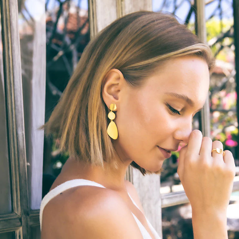 Woman wearing yellow earrings and a ring, outdoors.