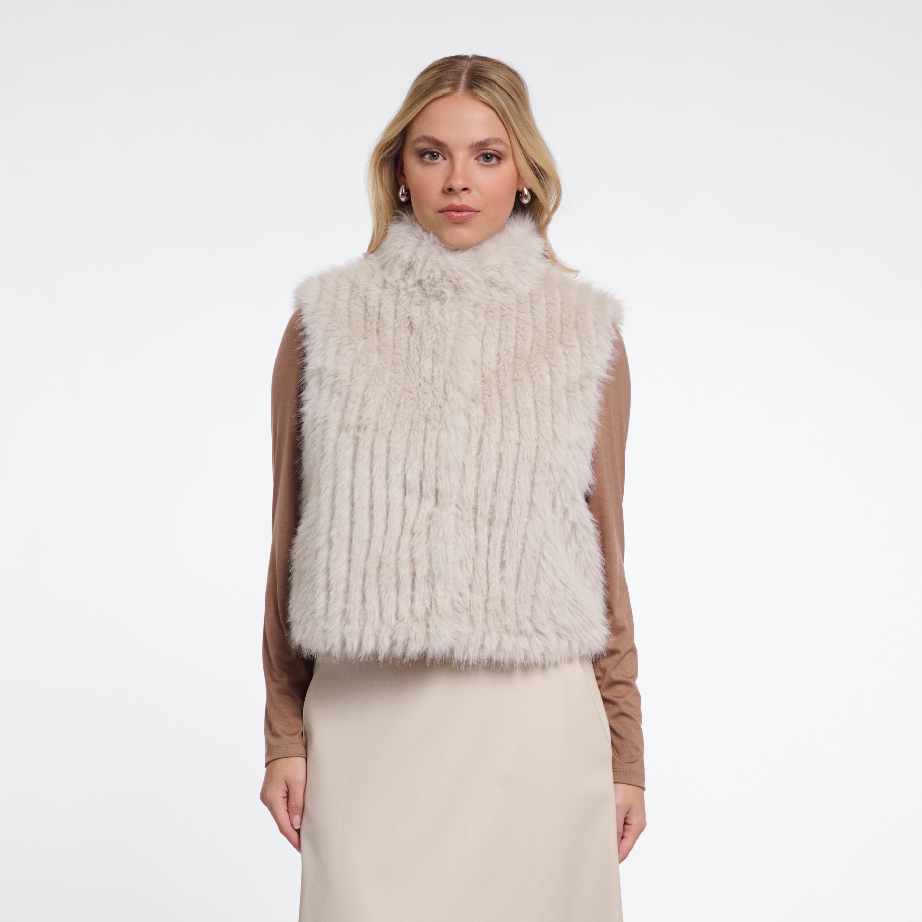 Woman wearing a cream fur vest over a long cream dress on a white background