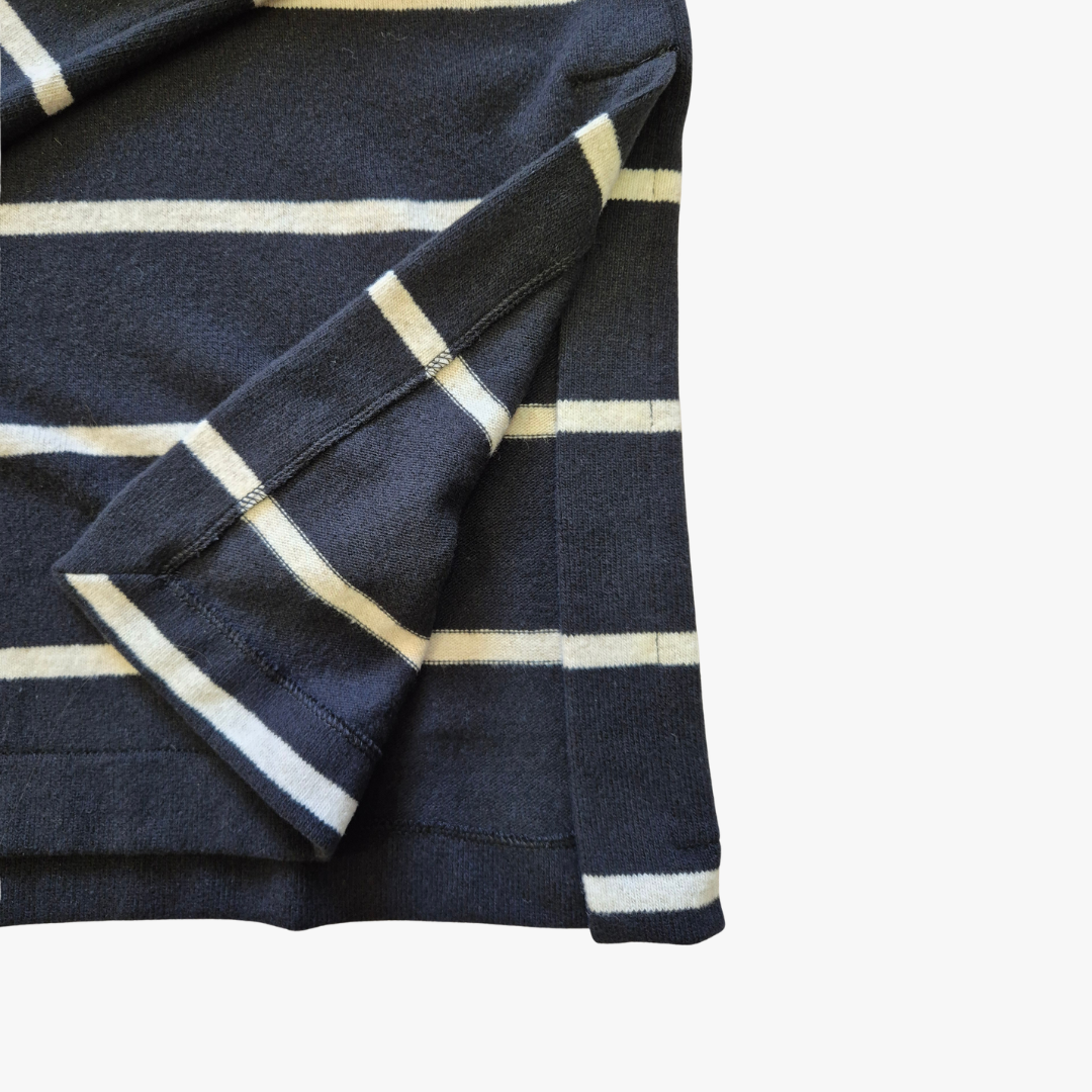 A close-up of a navy blue knit garment with horizontal cream stripes, showing the fabric texture and folded cuff detail against a plain white background.