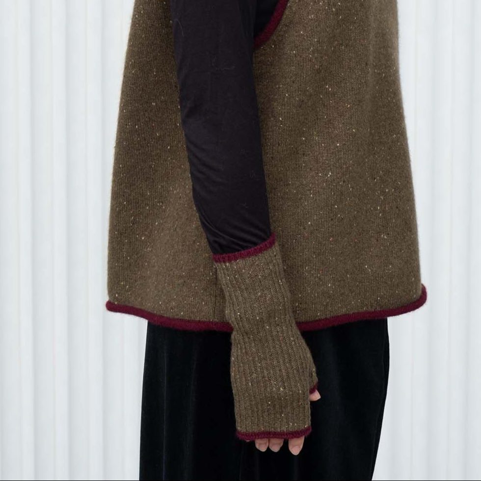 Woman wearing a brown knitted vest and hat against a white background