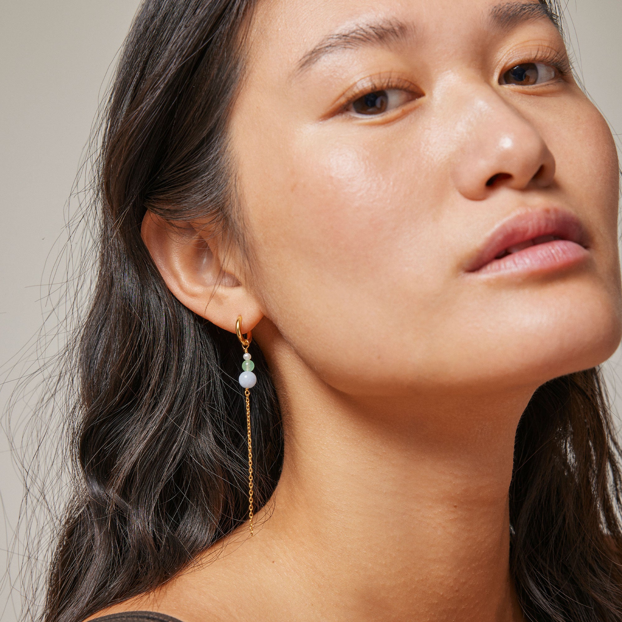 Gold hoop earrings with a delicate chain and small light-blue, green, and white beads dangling below.
