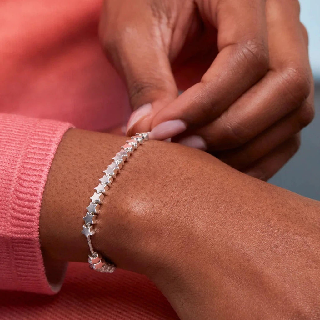 Silver star charm bracelet on a wrist.  The bracelet features a series of small, star-shaped charms connected by a thin cord.