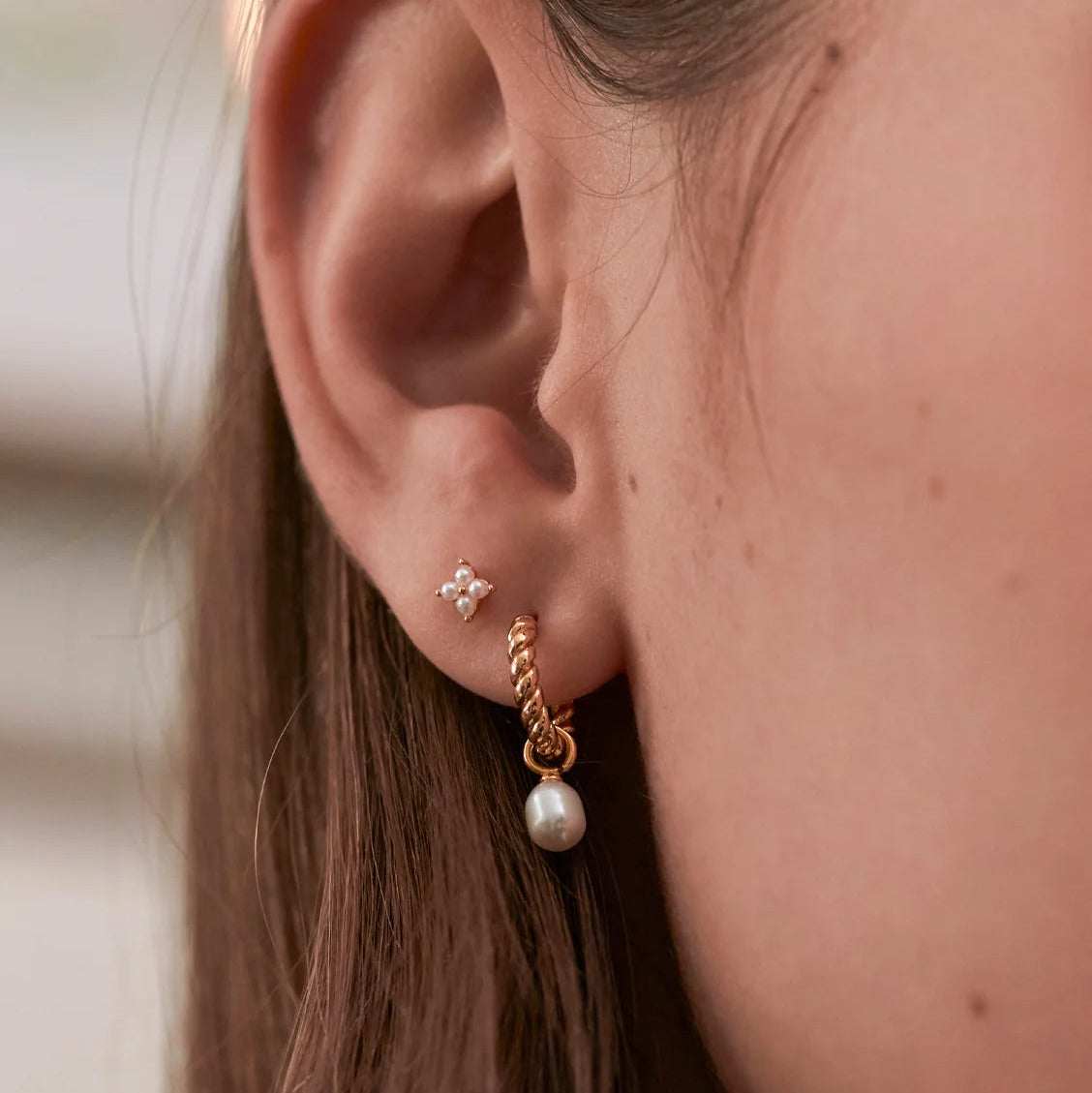 Close-up of an ear wearing a gold earring with a pearl drop.