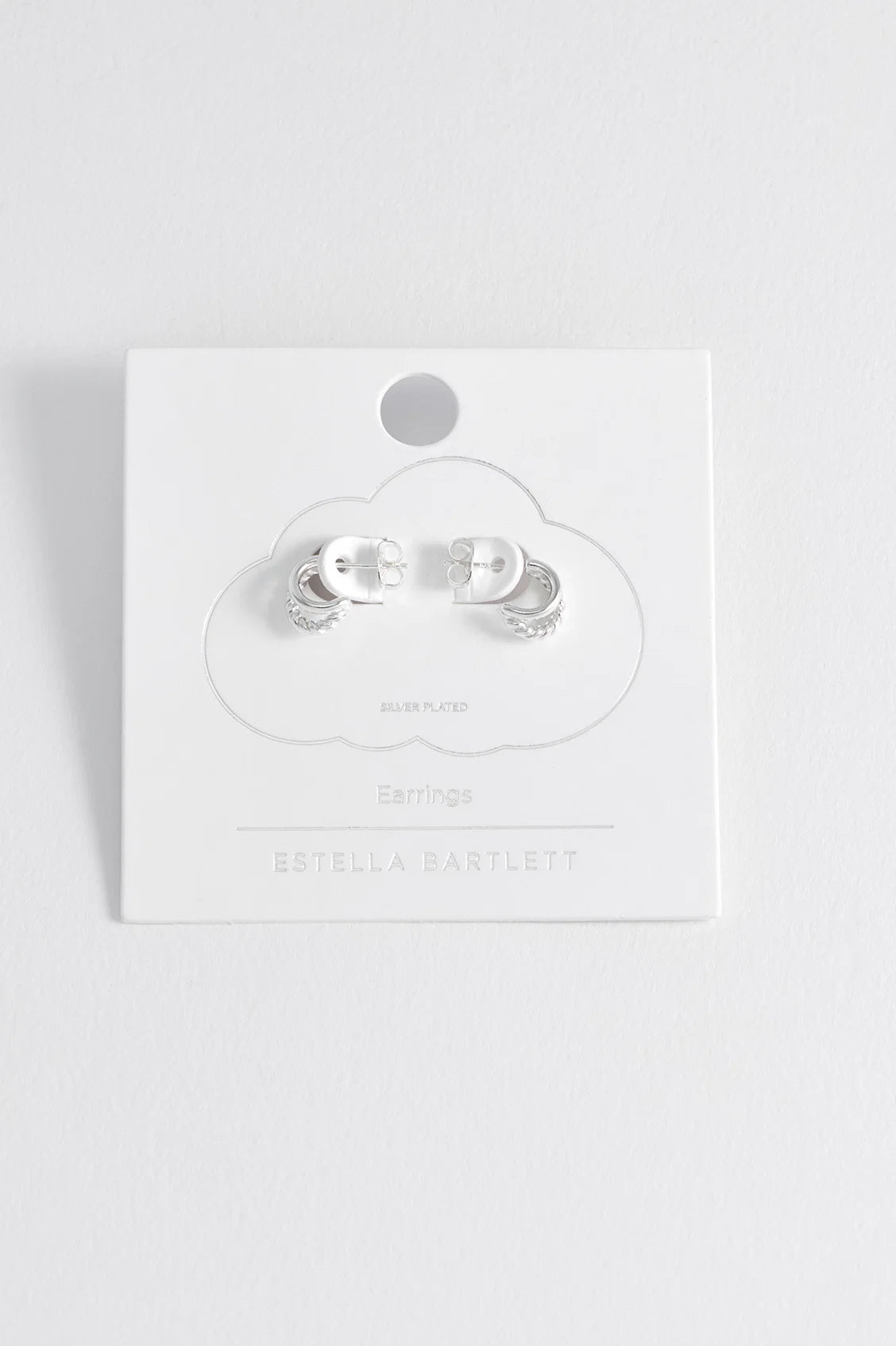 A pair of silver-toned hoop earrings displayed on a white cloud-shaped backing card labeled Estella Bartlett, photographed against a clean white background.
