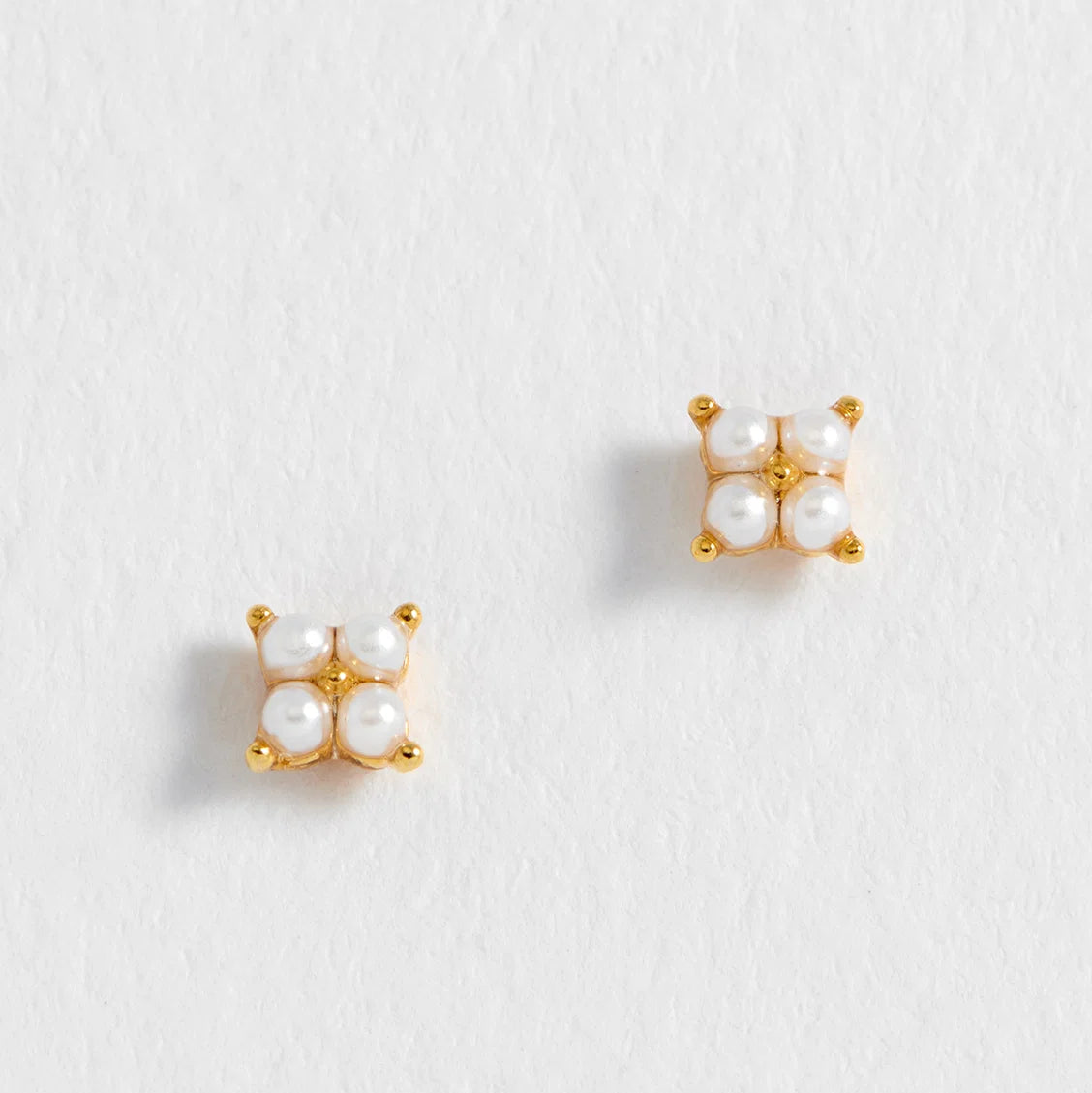 Pair of gold earrings with pearl-like stones on a light gray background