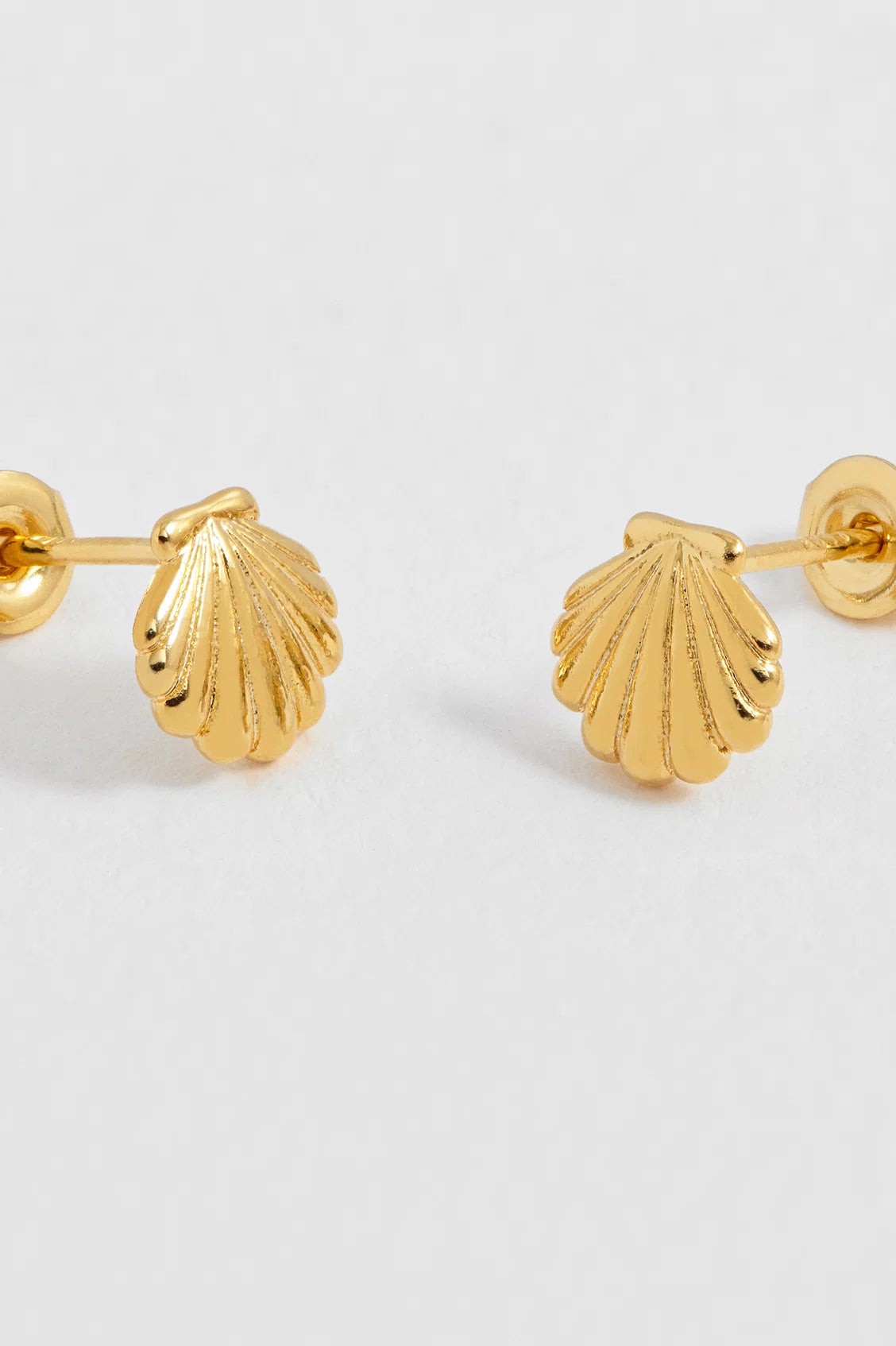 A pair of gold stud earrings shaped like textured scallop shells, shown on a plain light gray background.