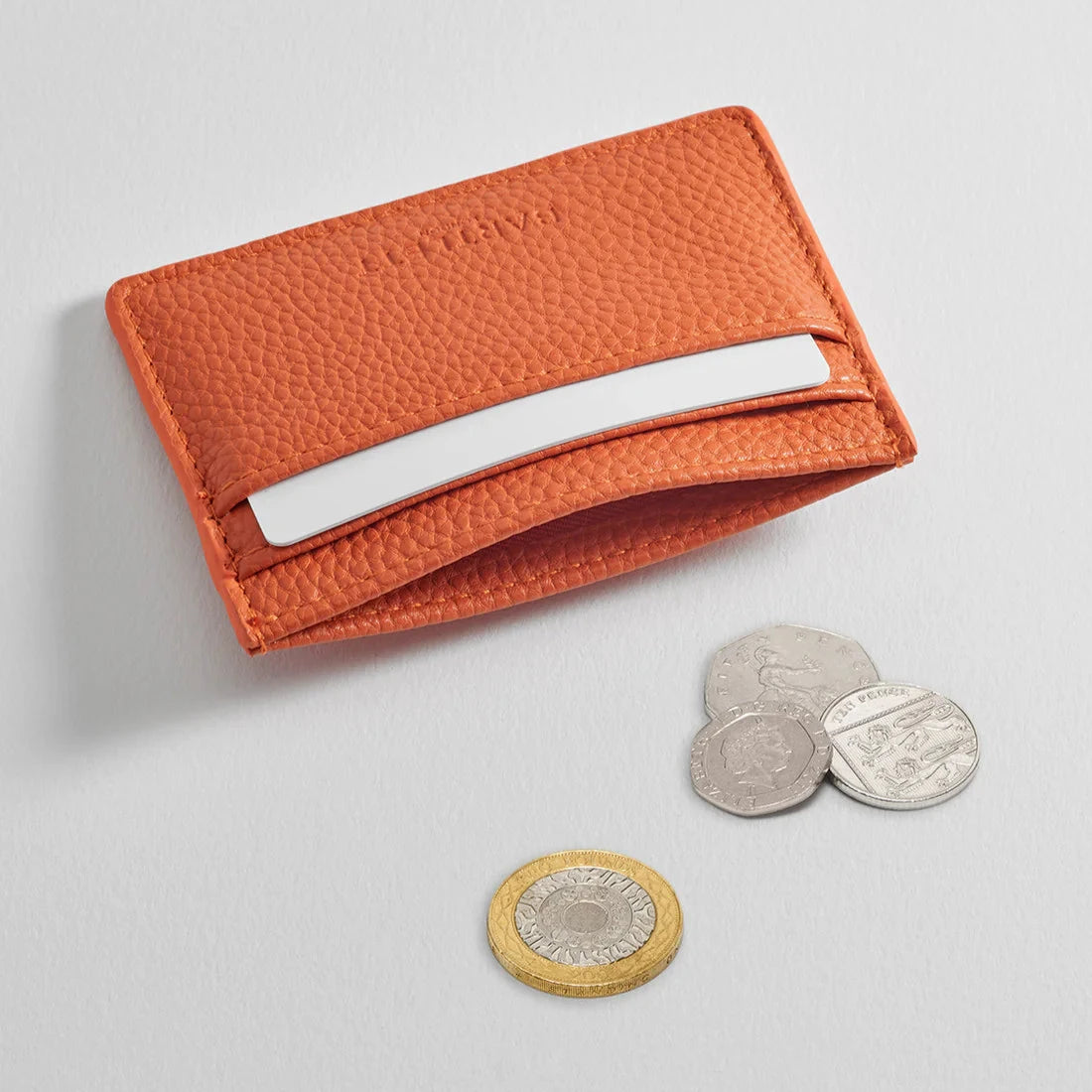 Orange leather card holder with a textured surface and a single card slot.  A few coins are nearby.