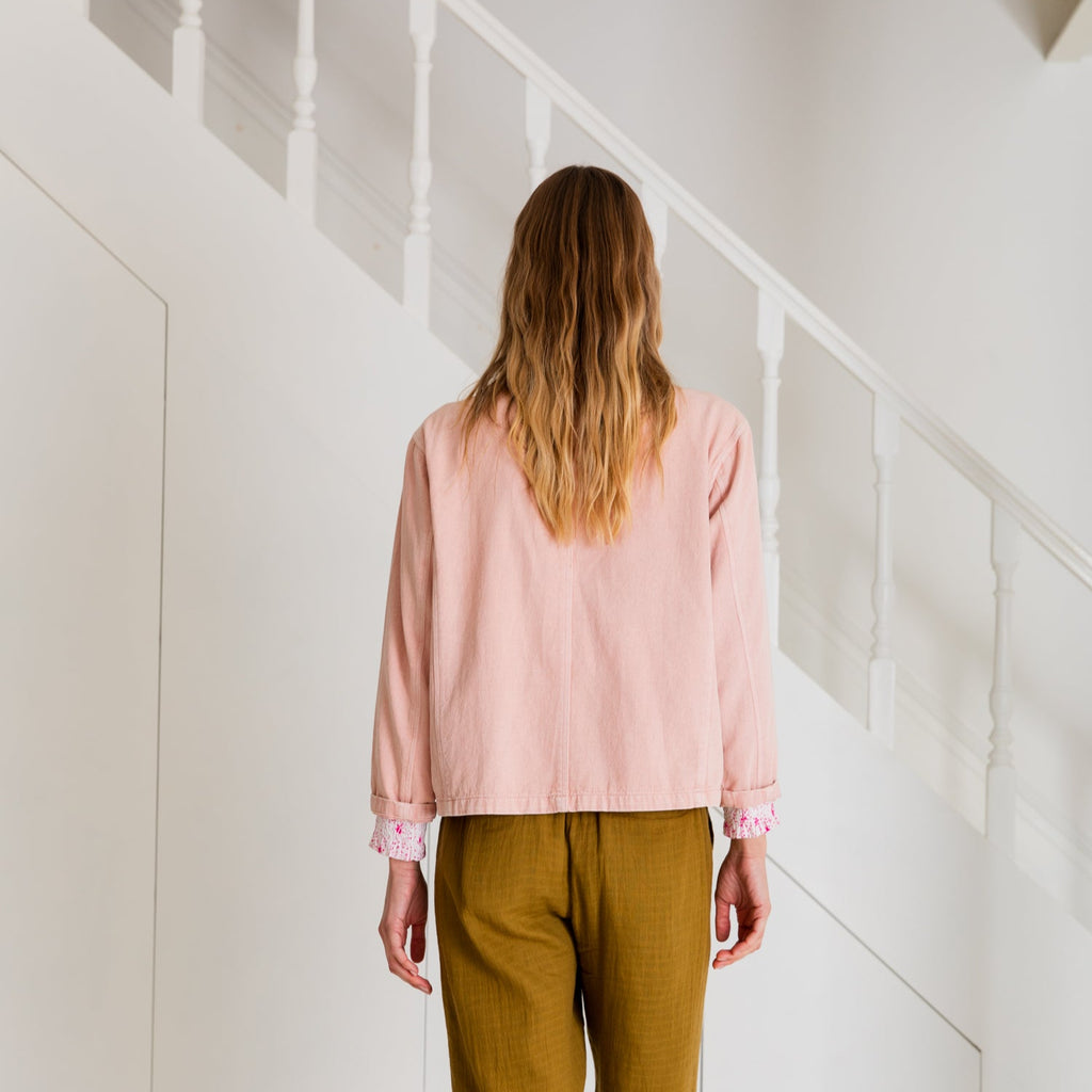 Back view of a person wearing Bonte's pink jacket and olive-green pants, standing near stairs.