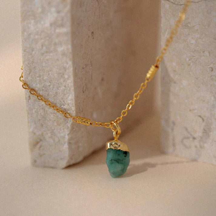 Gold necklace with a green pendant on a neutral background
