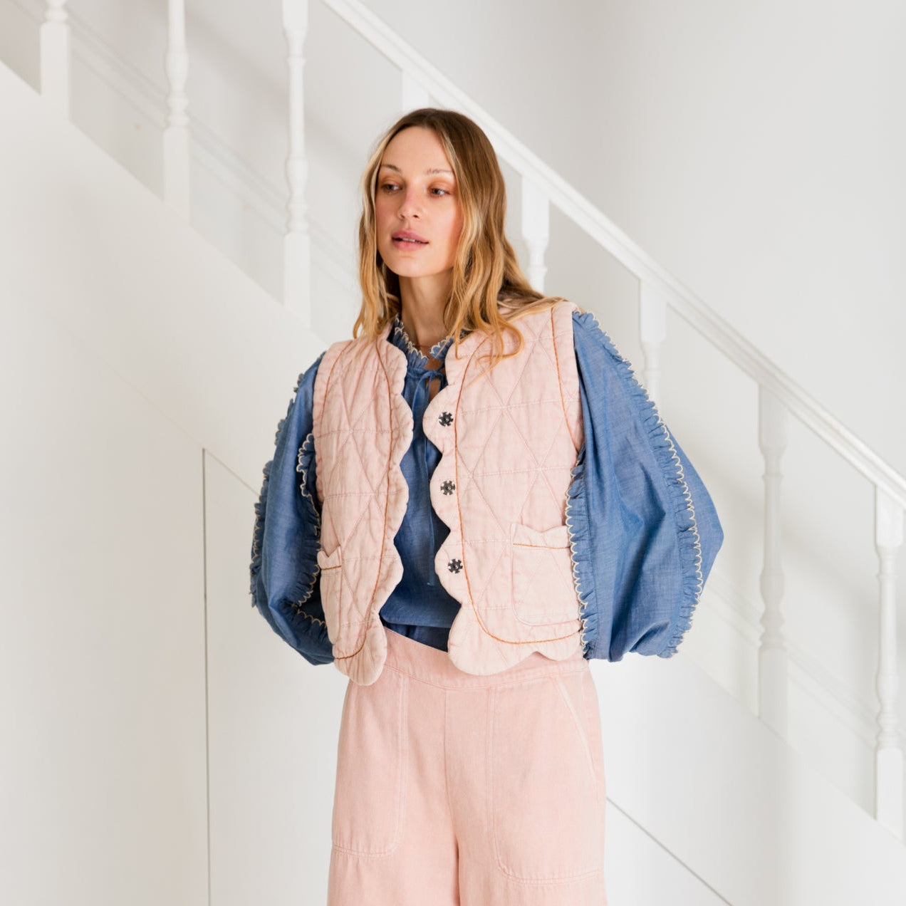 Pink quilted vest with scalloped edges, worn over a blue ruffled blouse and pink pants.