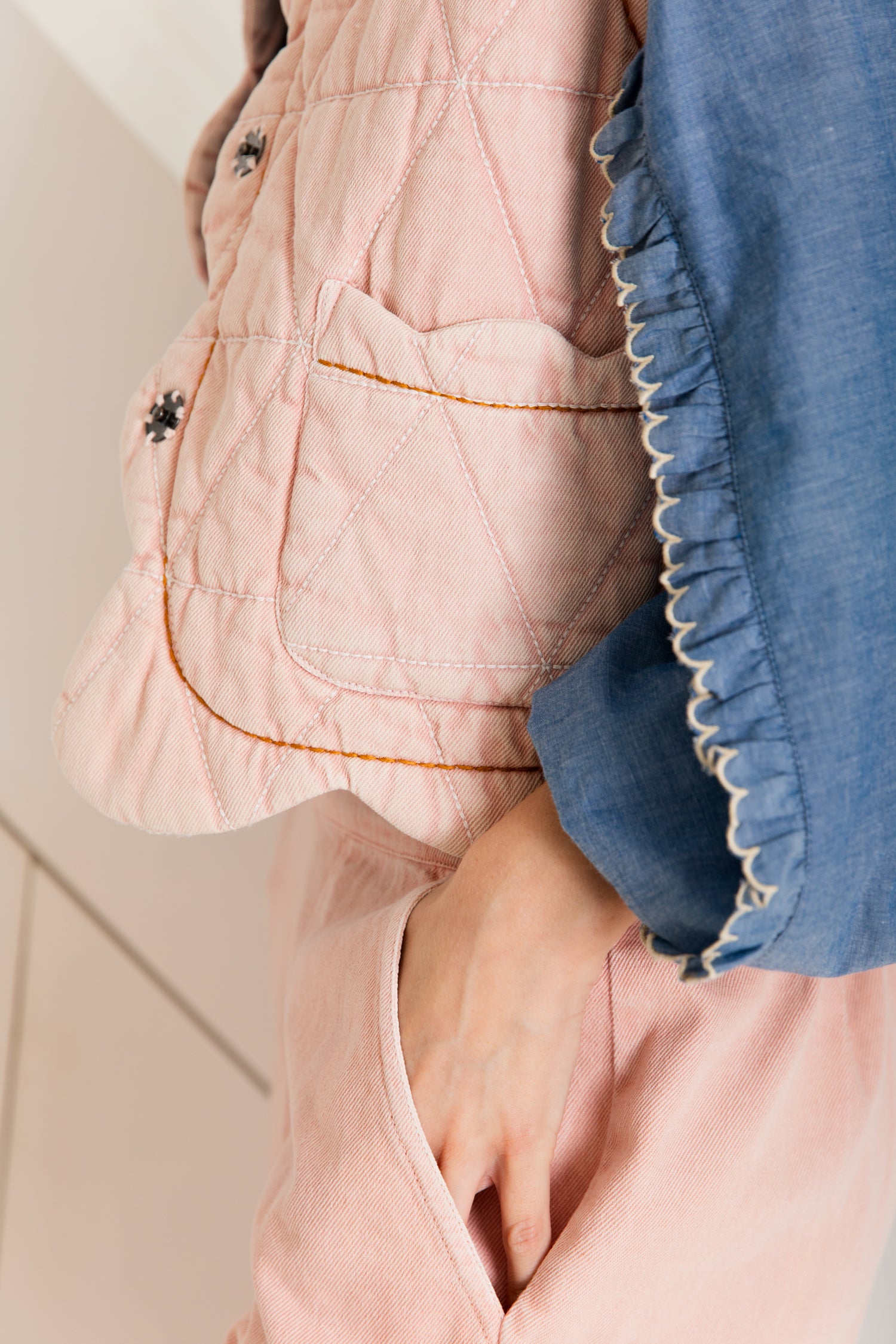 Pink quilted vest with orange stitching detail and a front pocket.