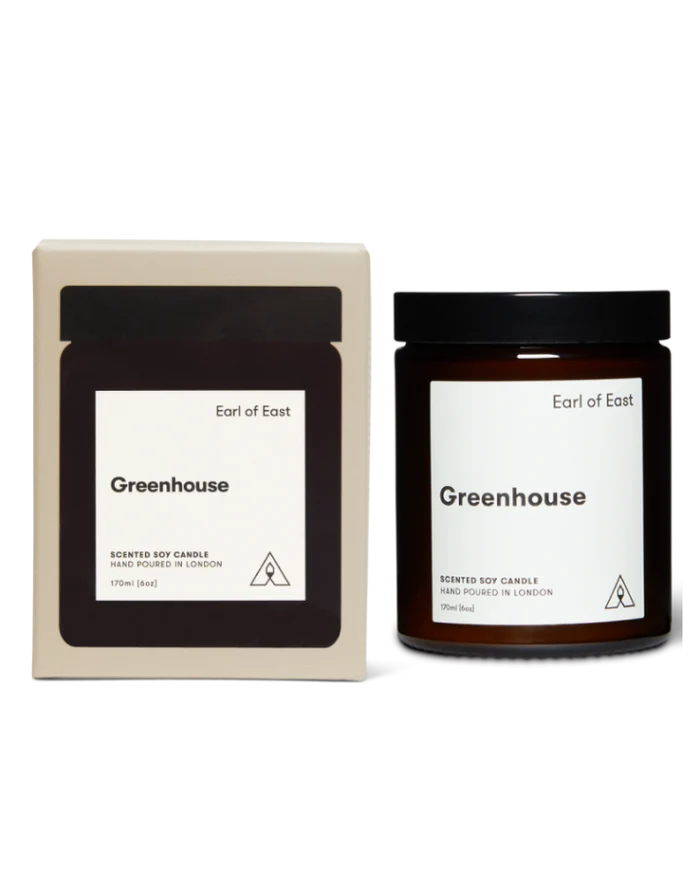 Earl of East Greenhouse scented soy candle shown with its cream-colored outer box and the amber glass jar candle with a black lid on a white background.
