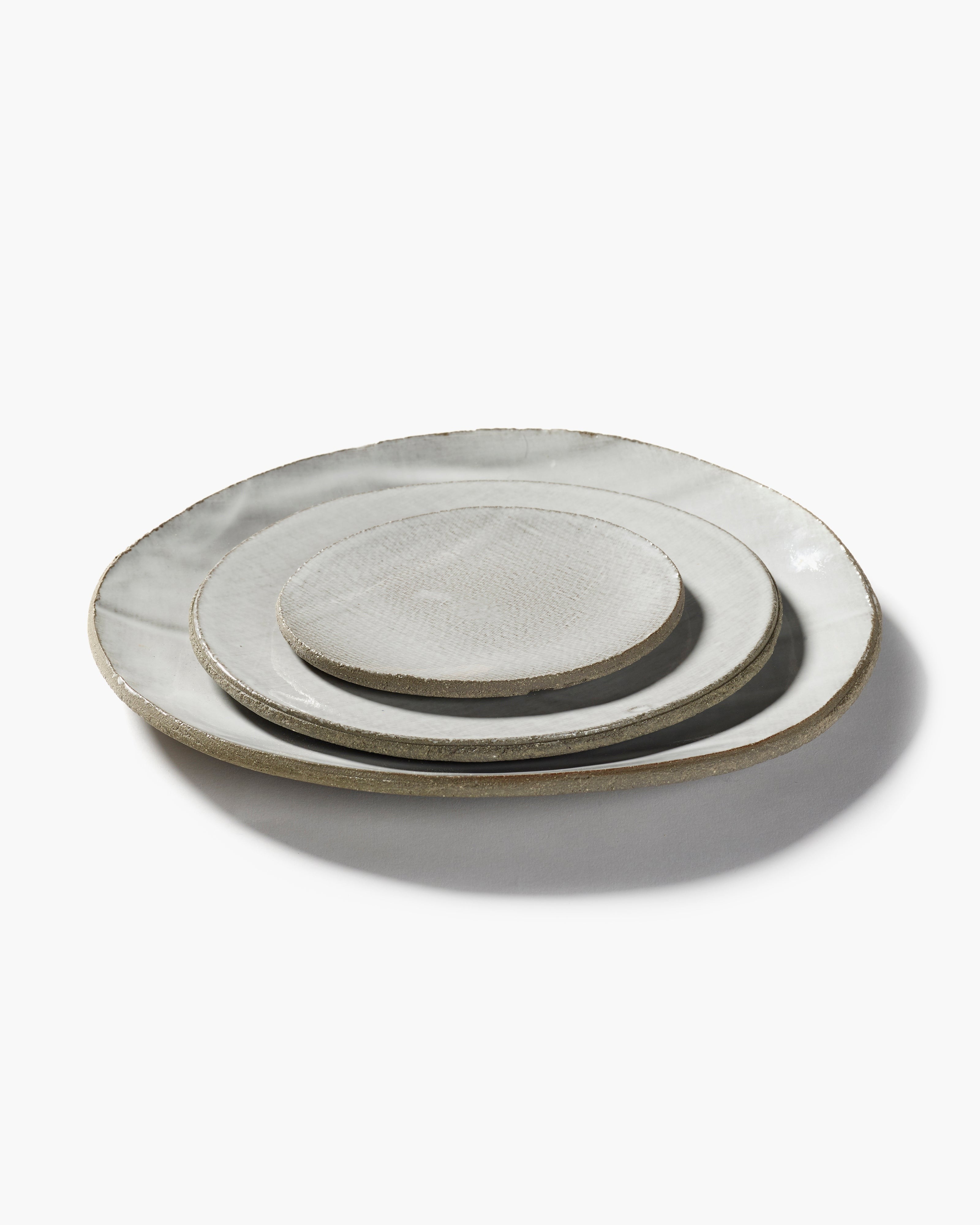 Three off-white ceramic plates of varying sizes stacked, each with a slightly textured surface and a darker gray rim.
