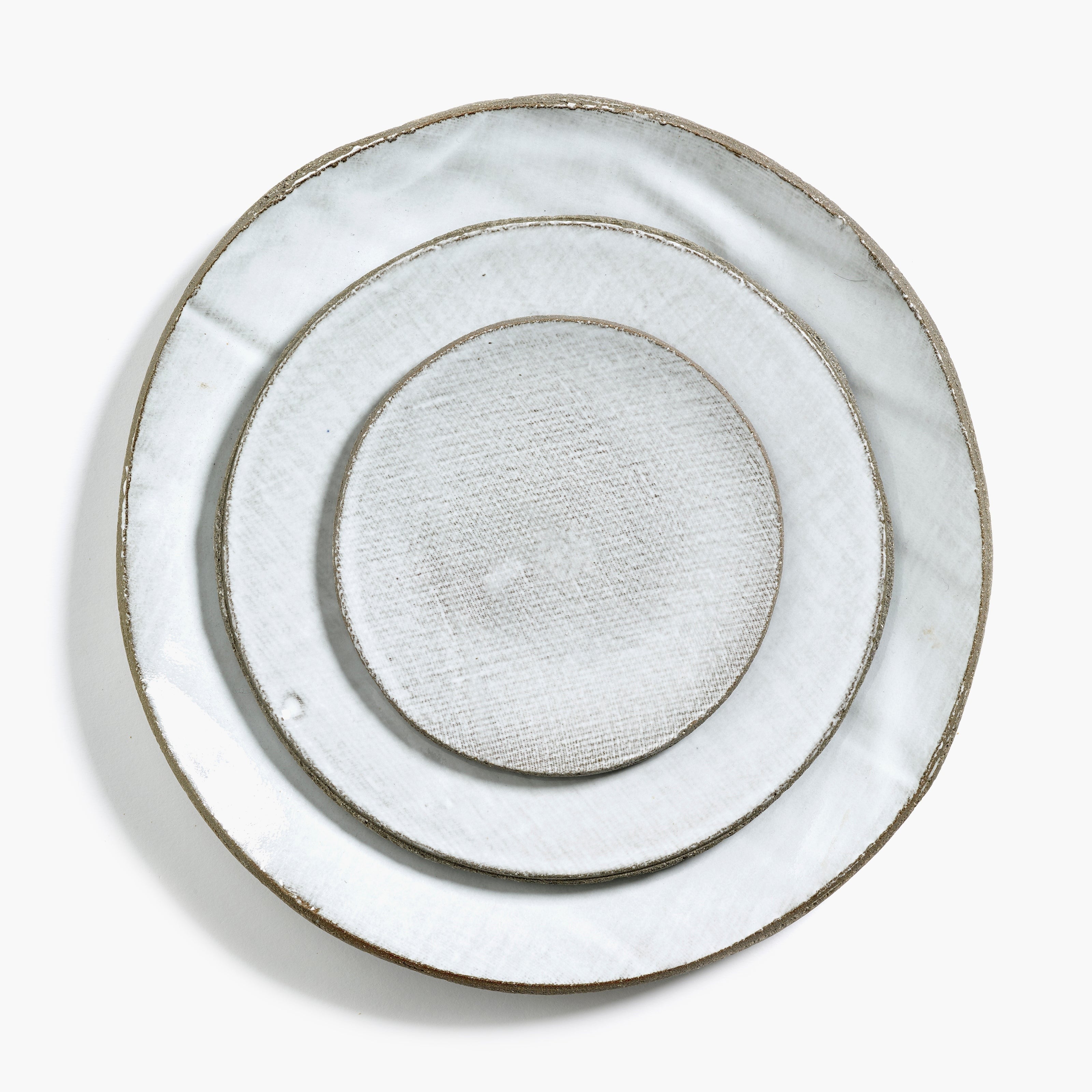 Three off-white ceramic plates, nested, with a textured surface and dark gray rims.