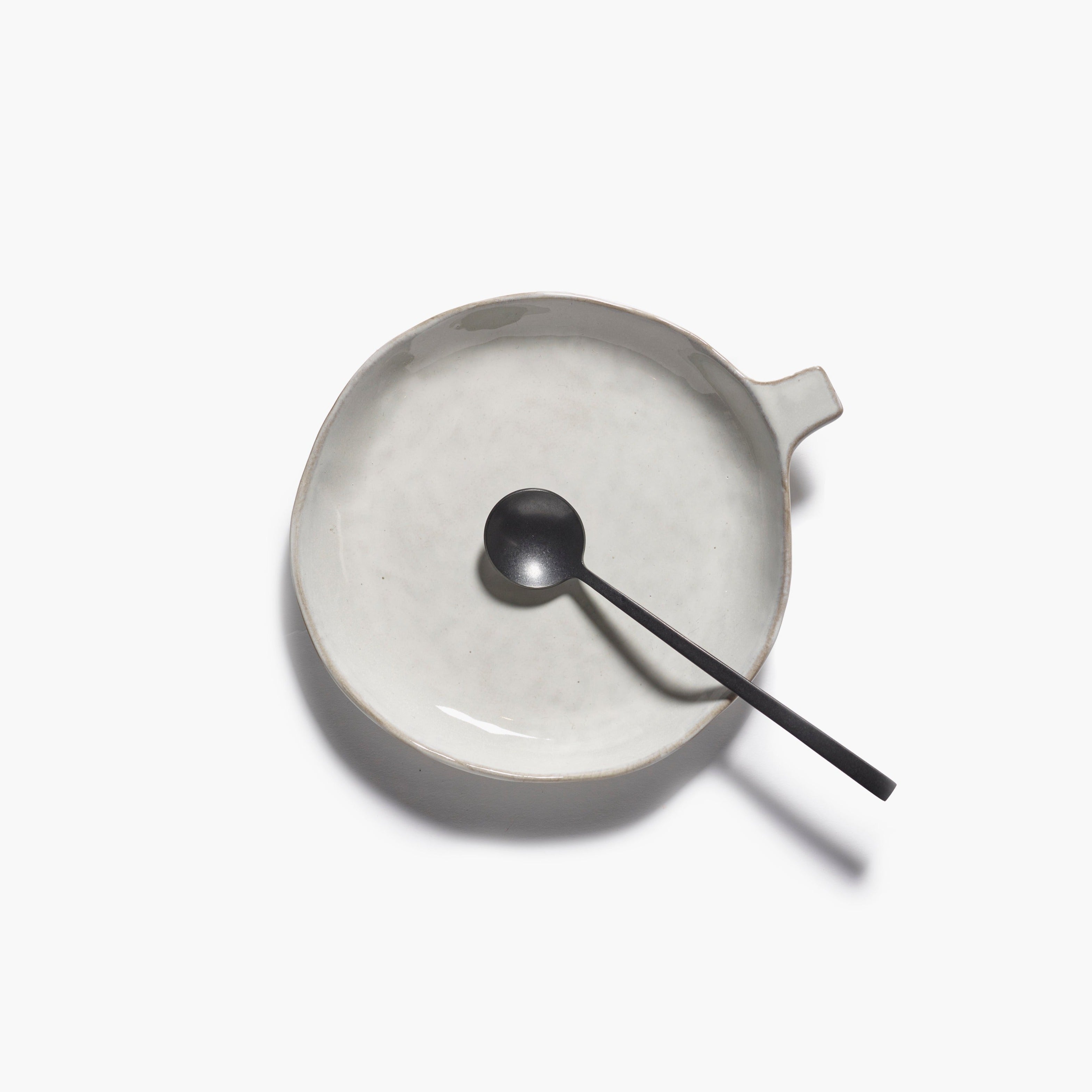A light gray ceramic dish with a small handle, featuring a textured surface, rests on a white background alongside a black