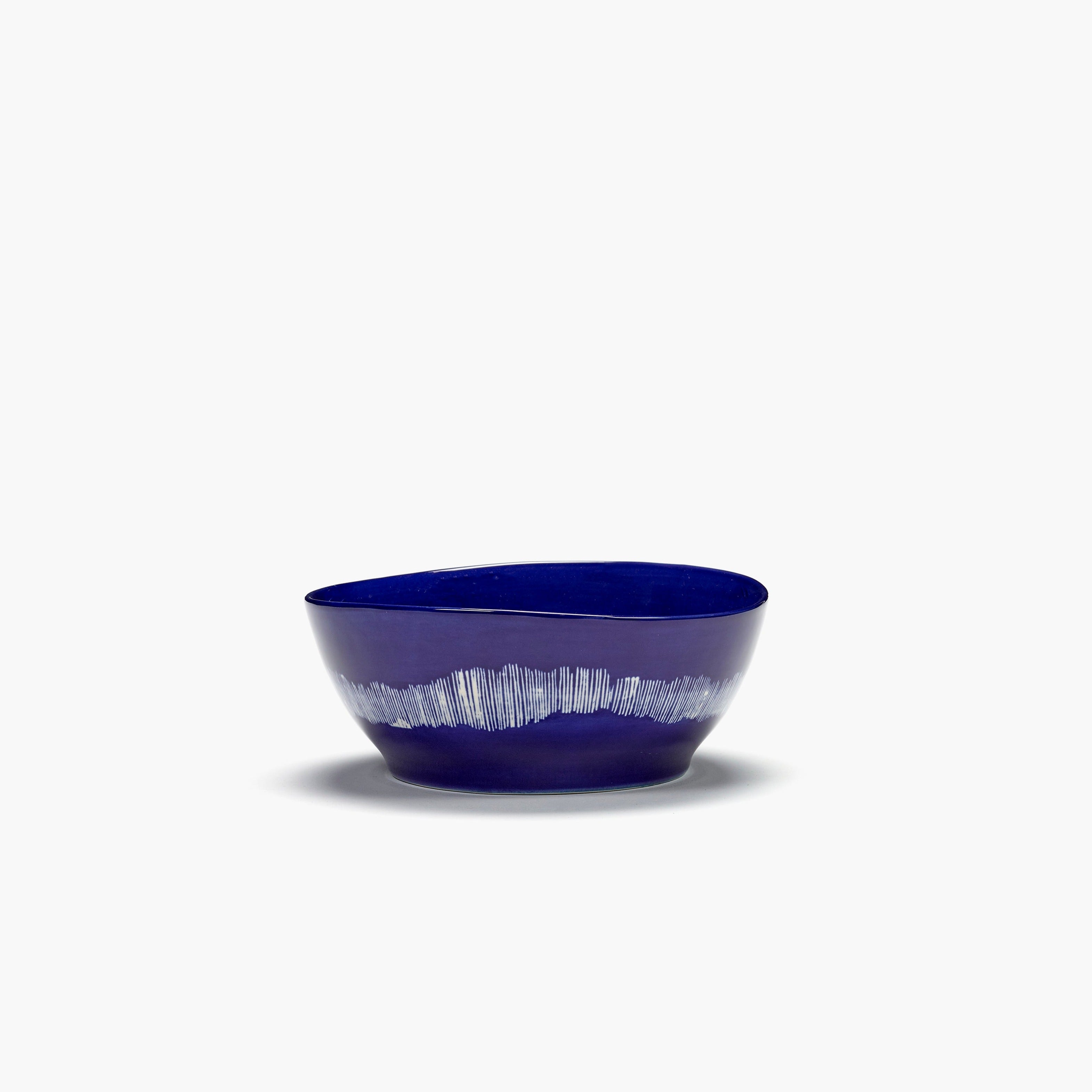 Cobalt blue ceramic bowl with irregular shape and white vertical line pattern near the base.