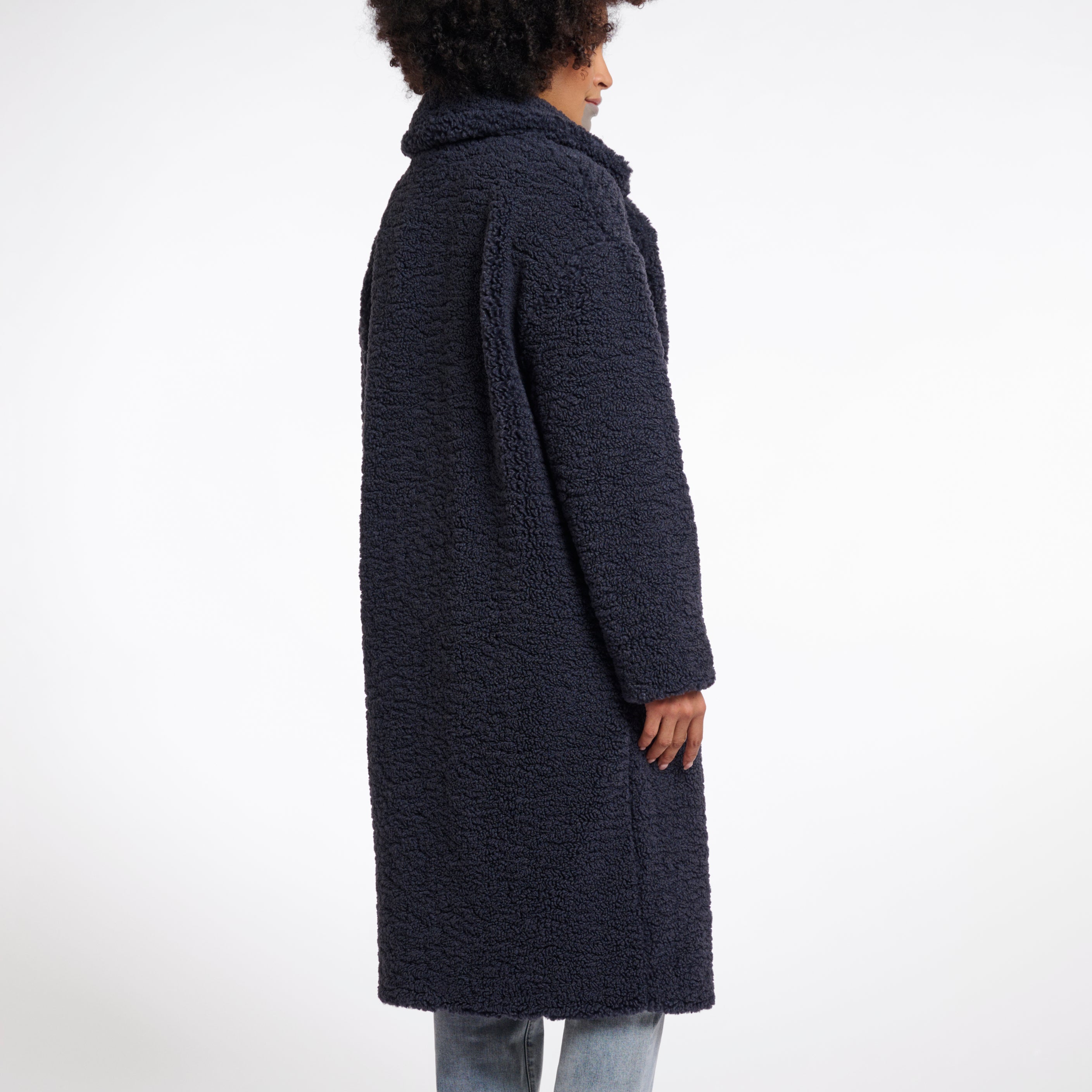 A woman models a double-breasted, teddy coat in night grey with a large lapel collar and side slit pockets.