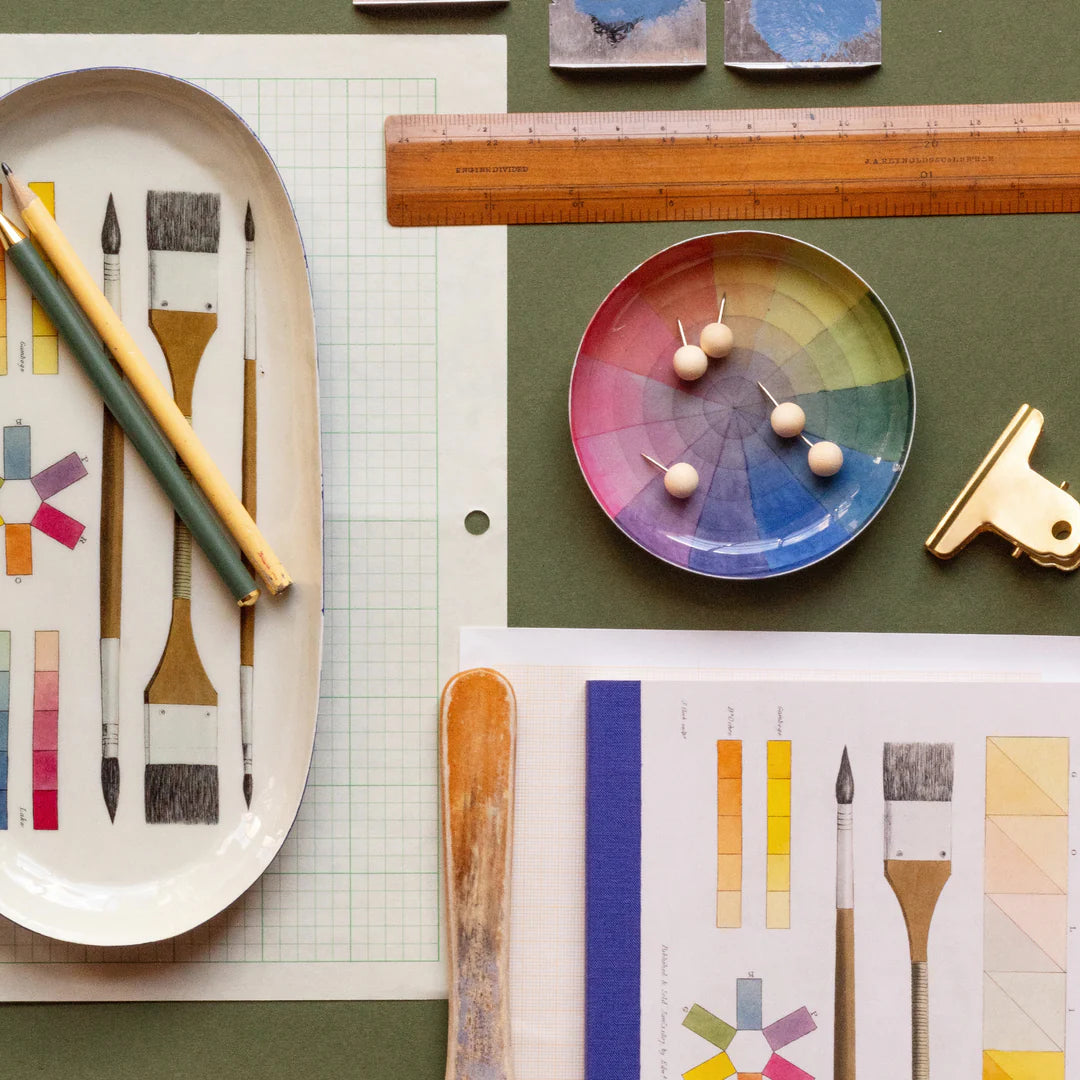 Art supplies including brushes, a color wheel, and a ruler on a green surface.