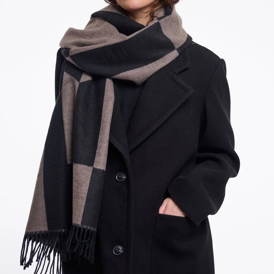 Woman wearing a black coat and a large black and brown checkered scarf on a white background