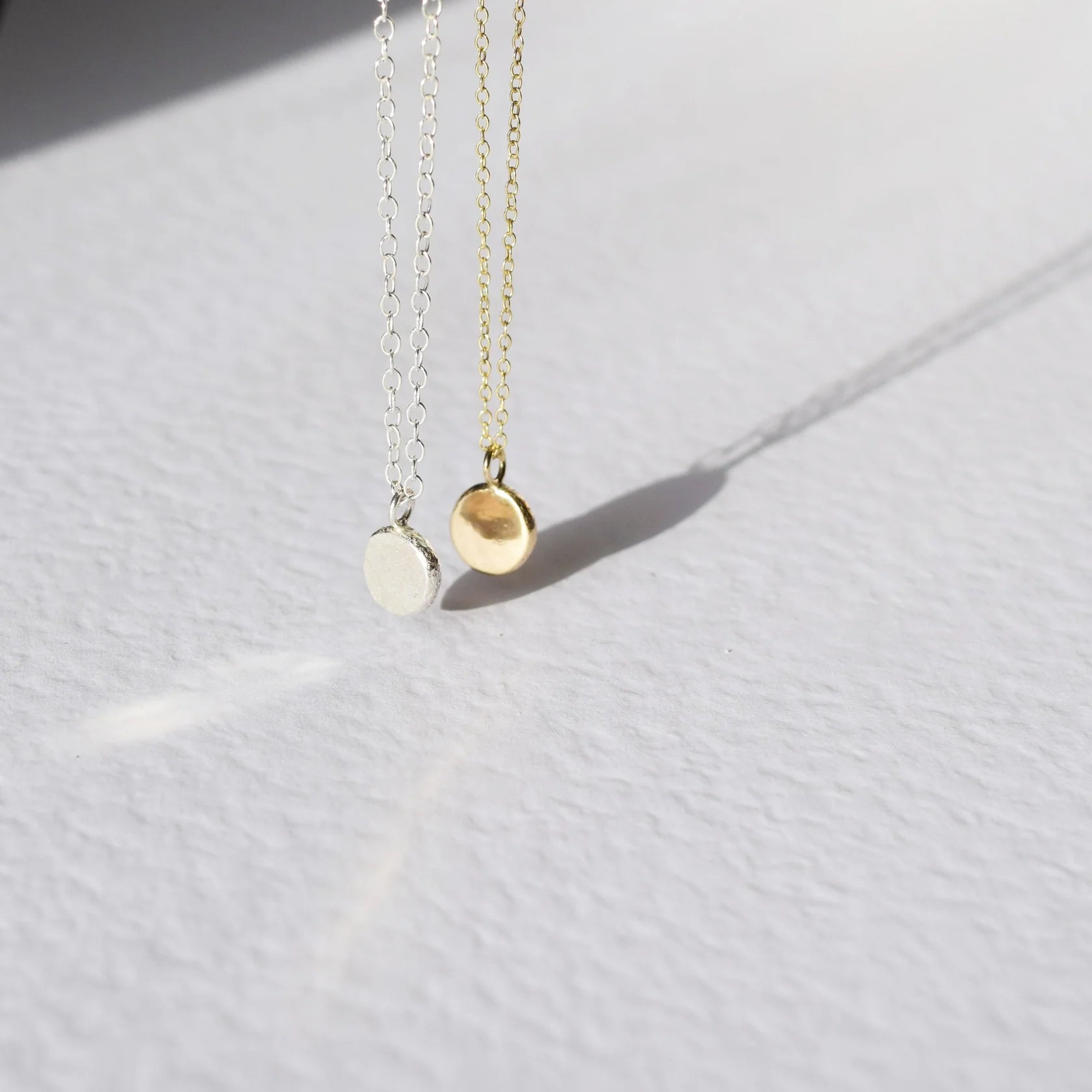 Two gold necklaces with round pendants on a light gray background