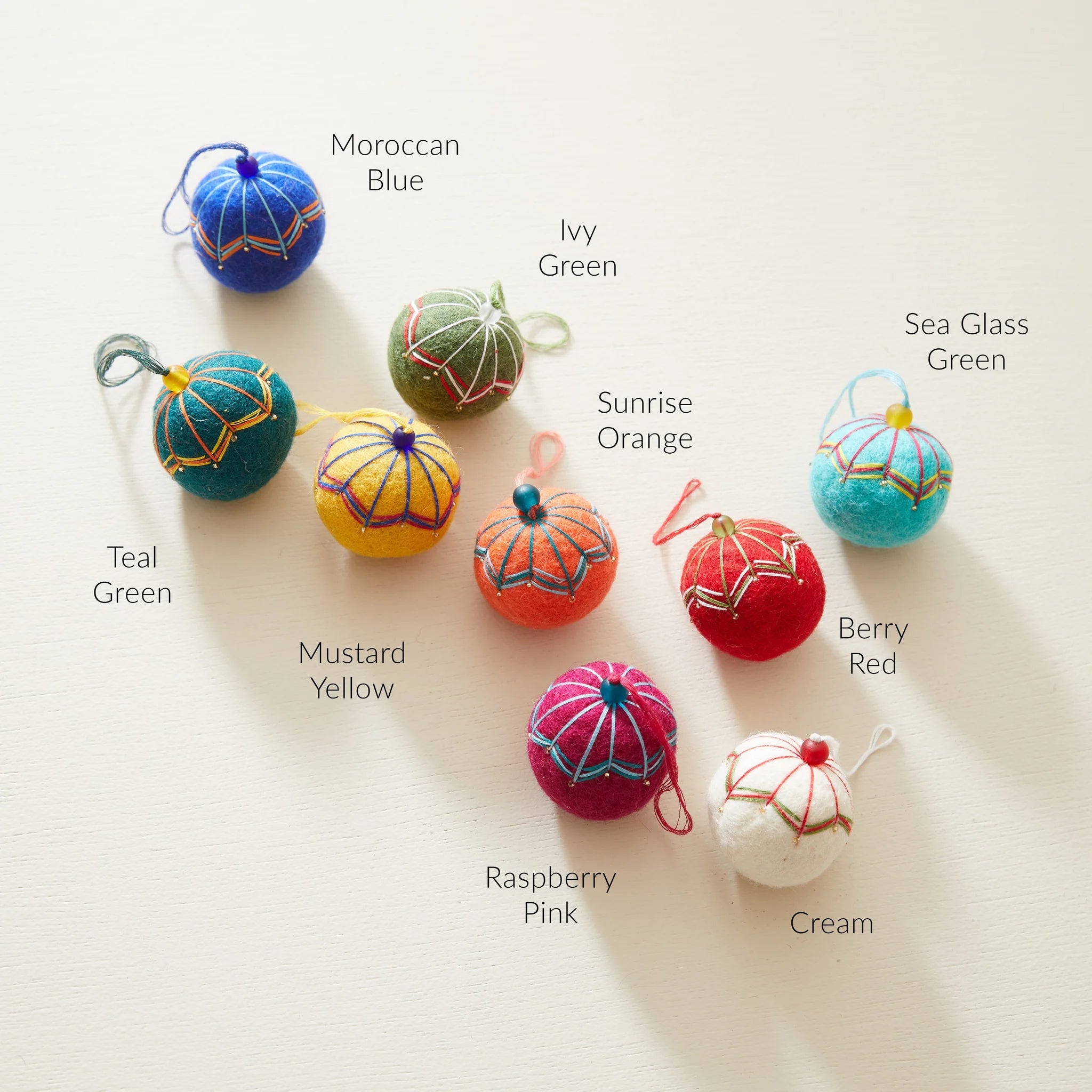 Collection of ten felt ornaments in various colors; each features embroidered detailing and a small hanging loop.
