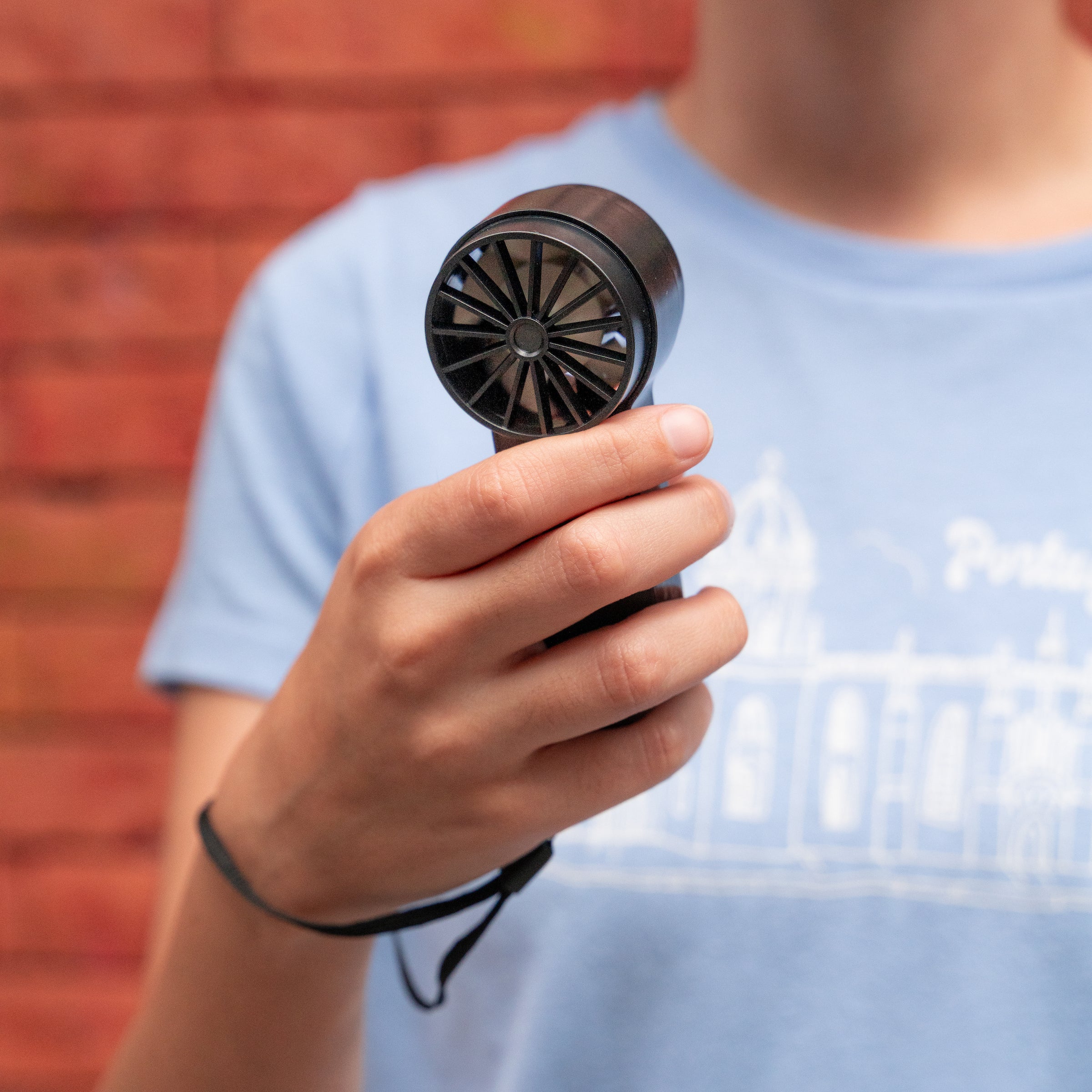 A person holds a small, black handheld fan with a visible, multi-bladed impeller.