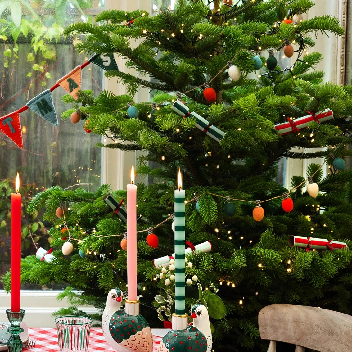 Decorated Christmas tree with candles and festive decorations in a home setting.