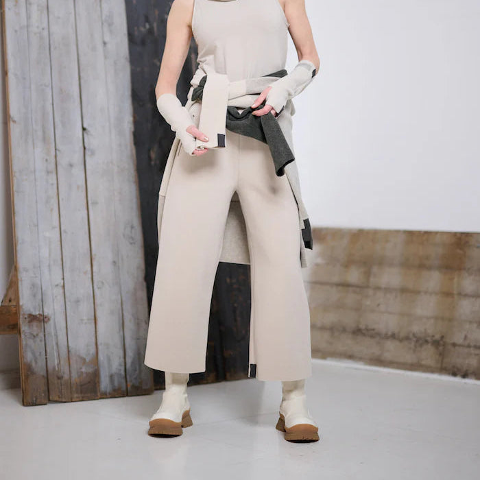 Woman wearing a beige outfit with a large bag against a rustic wooden backdrop