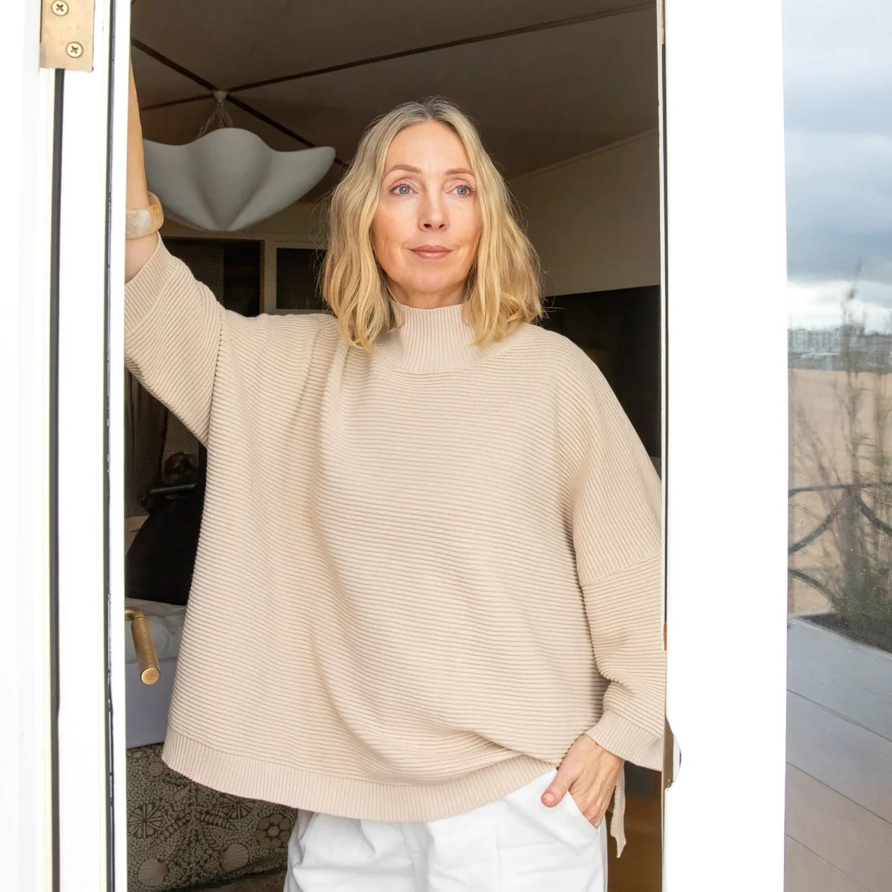Woman wearing a beige sweater standing in a doorway.