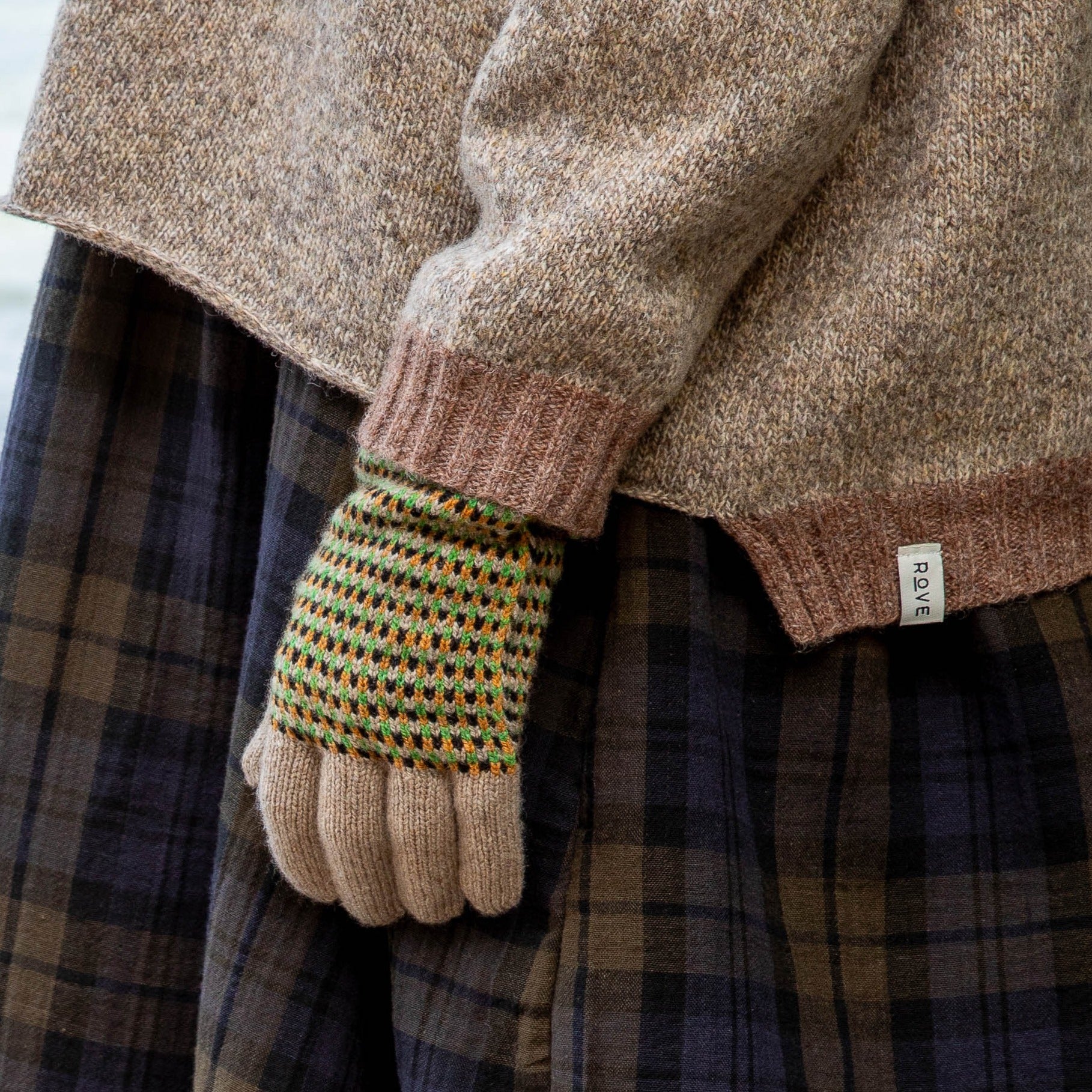 Close-up of a beige fingerless glove with a green, orange, and black geometric pattern on the back.